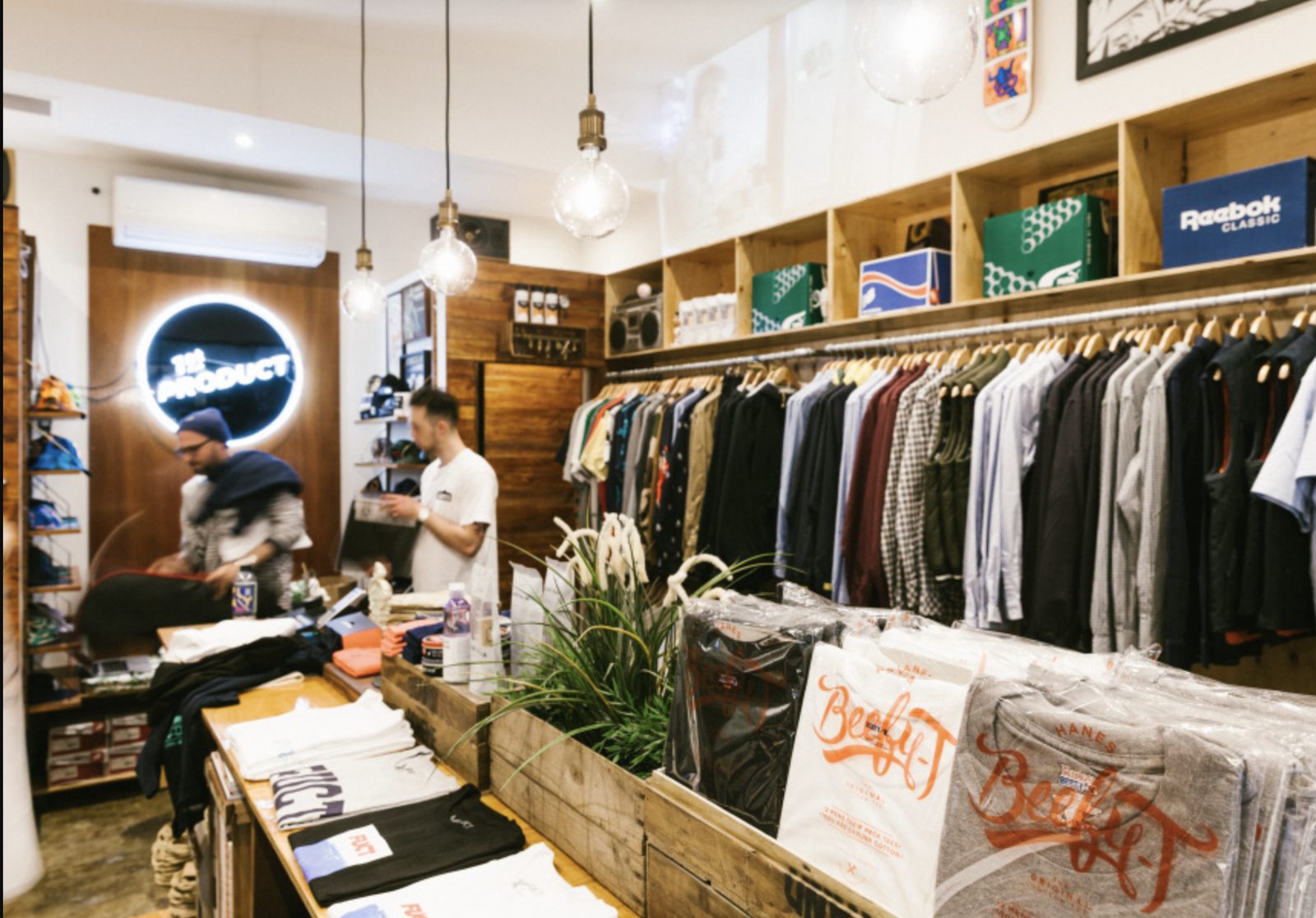 Inside 1st PRODUCT in Lido Arcade — racks of menswear beneath the shop's neon sign