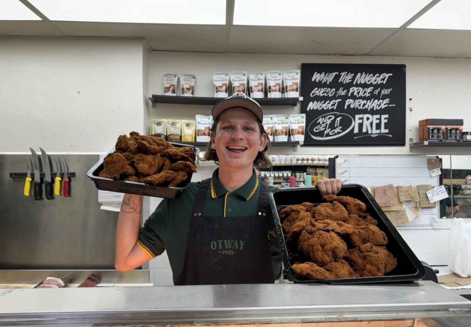 A smiling butcher at Glenferrie Gourmet Meats holding up two trays of crumbed chicken