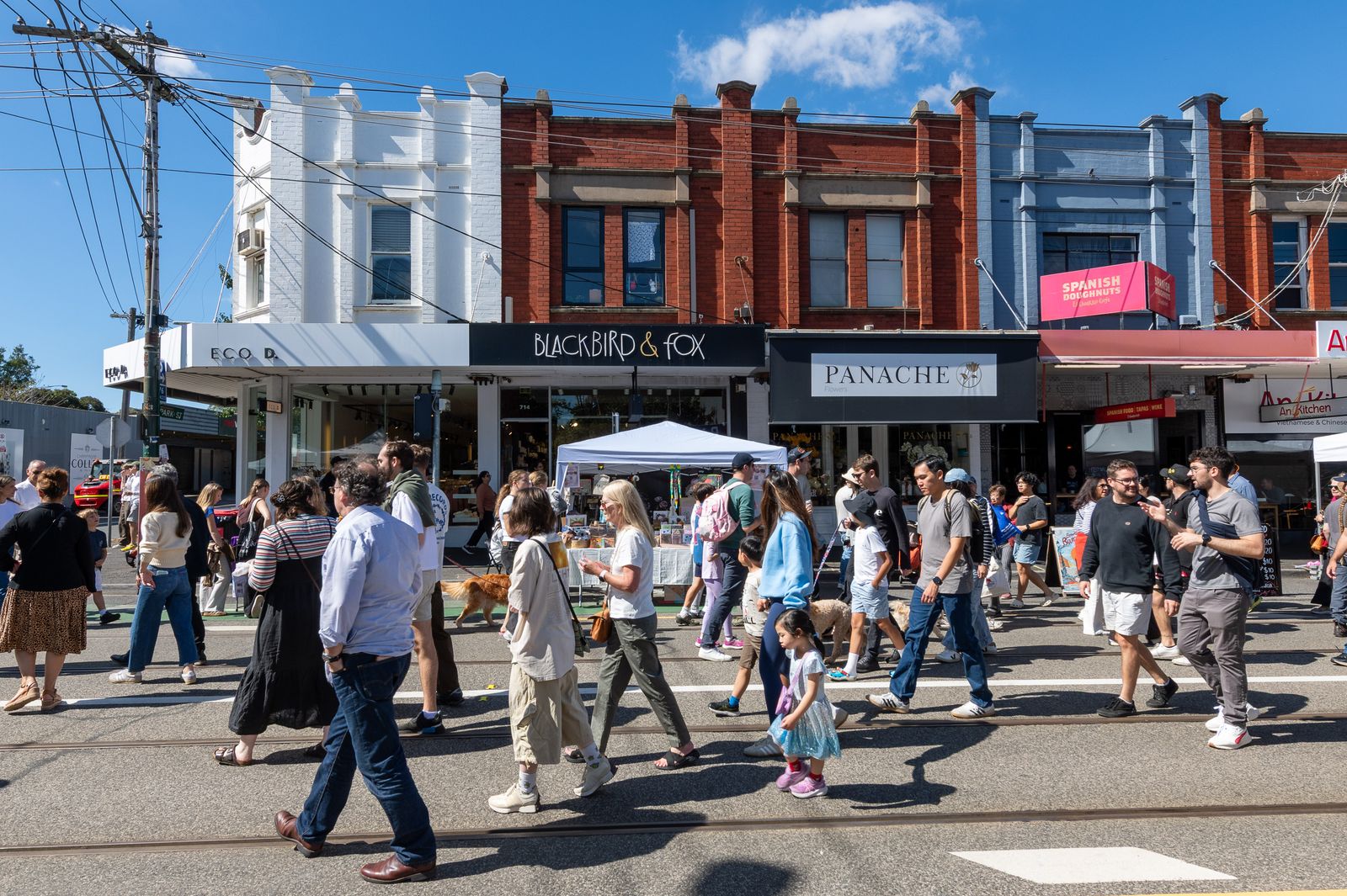 Festival-goers strolling past the heritage shopfronts of Glenferrie Road
